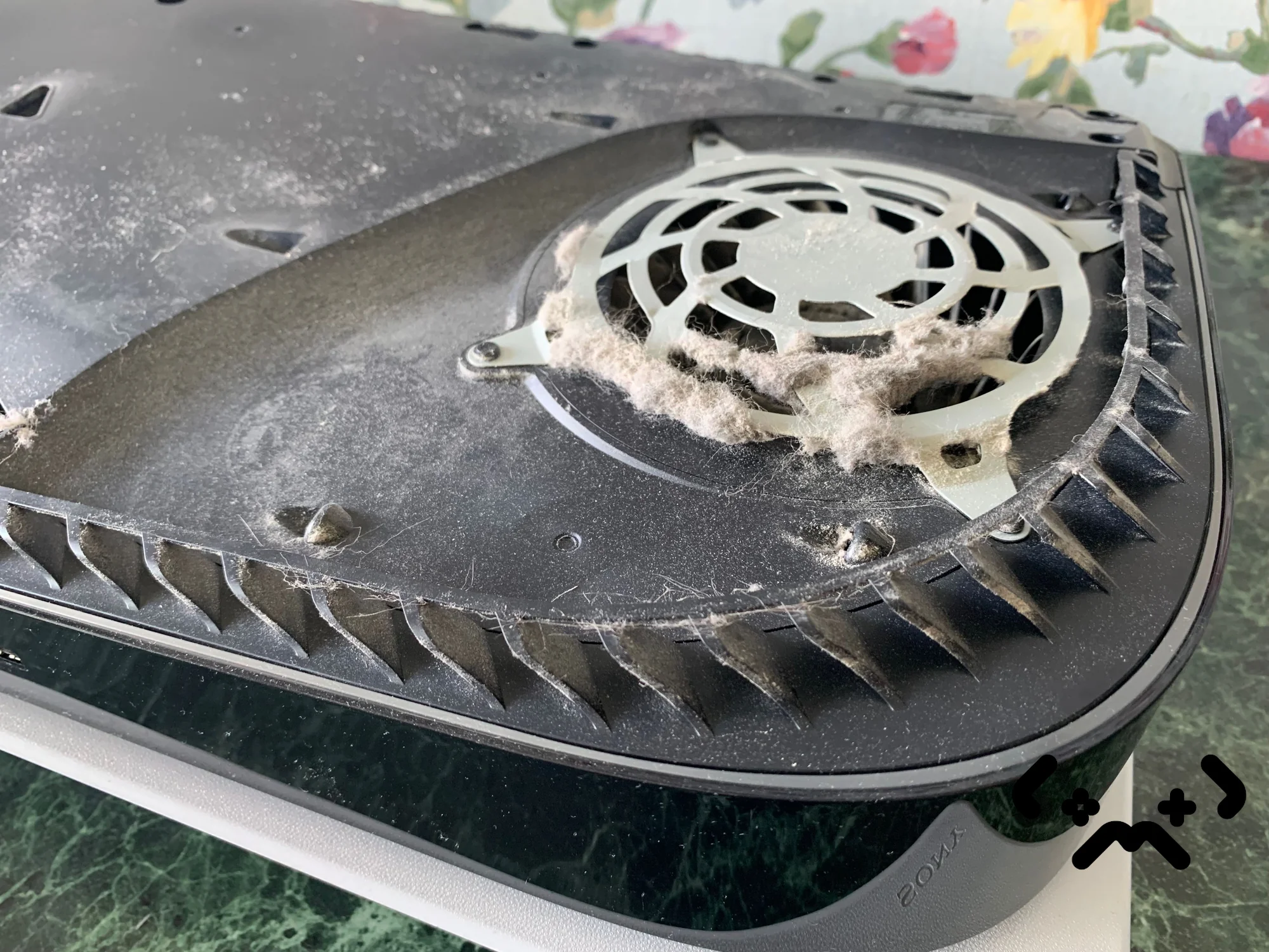 PS5 levymalli takakansi avattuna, ulospuhallusritilä paksun lemmikinkarvan ja pölymaton peitossa.